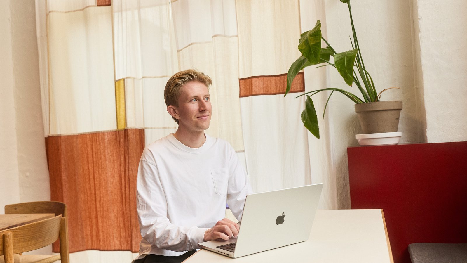 Christian Toft Bach ved laptoppen foran det vævede tekstil, med planten til højre
